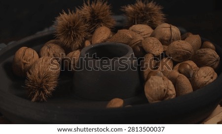 An eye level studio shot captures a variety of unpeeled nuts in a black ceramic bundt pan. Dramatic low key lighting emphasizes the deeply textured shells and organic autumn mood.