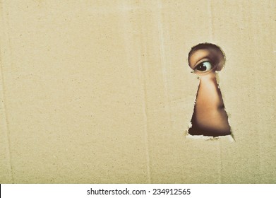 Eye looking through a conceptual keyhole on cardboard, close up