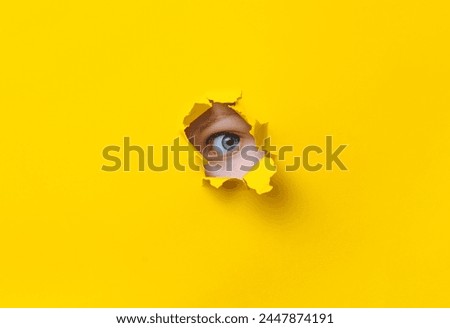 The eye looks into a hole in the yellow paper. The child watches his parents. A curious look. Jealousy, eavesdropping concept. Copy space. Stock fotó © 