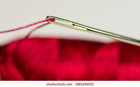 Eye Of The Needle With Red Polyester Thread. Spool Of Red Polyester Sewing Thread In The Background. Selective Focus. Bokeh.