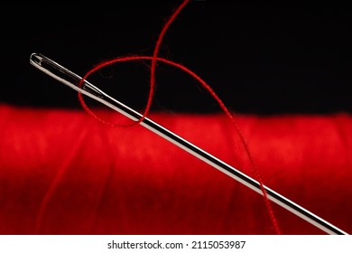 Eye Of The Needle With Red Polyester Thread. Spool Of Red Polyester Sewing Thread In The Background. Selective Focus. Bokeh.