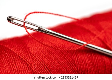 Eye Of The Needle With Red Polyester Thread. Spool Of Red Polyester Sewing Thread In The Background. Selective Focus. Bokeh.