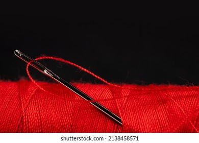 Eye Of The Needle With Red Polyester Thread. Spool Of Red Polyester Sewing Thread In The Background. Selective Focus. Bokeh.