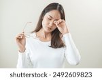 Eye problem concept, fatigue asian young woman tired eyes irritated rubbing, massage eye dry relief vision pain after work, eye strain, hand holding glasses, suffer bad blurry isolated on background.