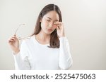 Eye problem concept, fatigue asian young woman tired eyes irritated rubbing, massage eye dry relief vision pain after work, eye strain, hand holding glasses, suffer bad blurry isolated on background.