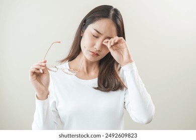 Eye problem concept, fatigue asian young woman tired eyes irritated rubbing, massage eye dry relief vision pain after work, eye strain, hand holding glasses, suffer bad blurry isolated on background. - Powered by Shutterstock