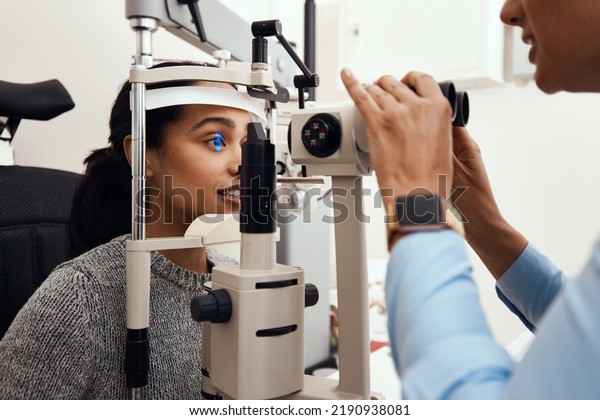 Eye test, exam or screening with an ophthalmoscope\
and an optometrist or optician in the optometry industry. Young\
woman getting her eyes tested for prescription glasses or contact\
lenses for vision