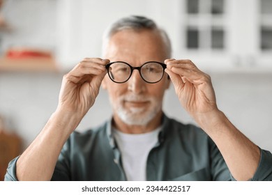 Eye Vision Concept. Smiling Senior Man Looking At Camera Through Eyeglasses In His Hands, Handsome Elderly Gentleman Trying New Glasses While Standing At Home Interior, Selective Focus - Powered by Shutterstock