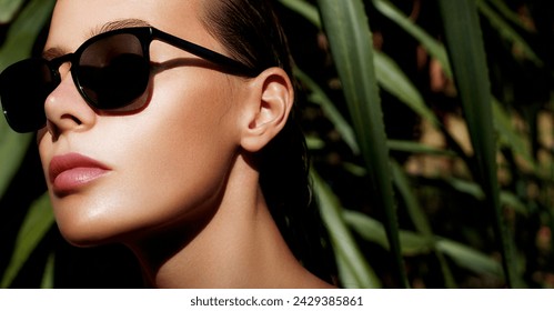 Eye wear fashion. Elegant woman wearing chic black square classic sunglasses, her skin glowing in natural light, set against a backdrop of lush tropical greenery. Stylish luxury sunglasses 
 - Powered by Shutterstock