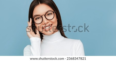 Eye wear fashion woman portrait. Beauty. Asian girl in a white polo neck and eyeglasses is looking at camera and smiling, on an blue background