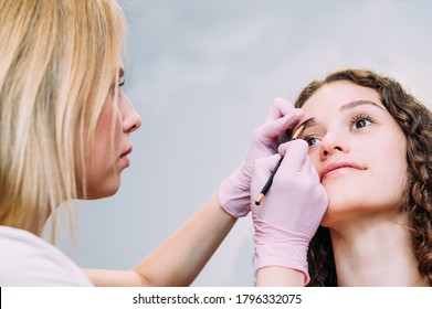 Eyebrow Master Draws The Shape Of The Eyebrows Of A Young Woman With An Eyebrow Pencil. Henna Eyebrow Coloring Procedure In A Beauty Salon