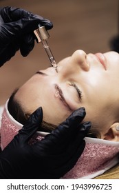 Eyebrow Microblading. Master In Black Gloves Drips Oil Onto The Model's Eyebrow