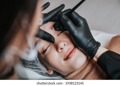 Eyebrows microblading concept, eyebrow permanent makeup procedure. Beauty expert is wearing shiled and protective face mask due to Coronavirus pandemic.