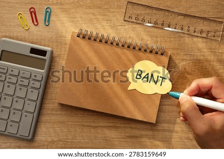 Eye-catching image of BANT text on stickynote. The word stands for Budget, Authority, Needs, Timeframe. Shown with pen, calculator, hand.