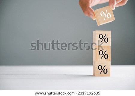 Eye-catching image capturing the concept of interest rate and mortgage rates. Businessman's hand putting a wood cube block with a percentage symbol icon, symbolizing the fluctuating nature of rates.