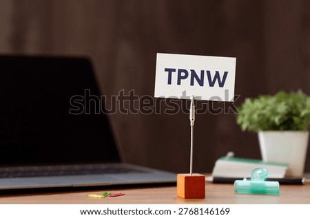 Eye-catching image of TPNW text on card. The word stands for Treaty on the Prohibition of Nuclear Weapons. Shown with laptop, clips.