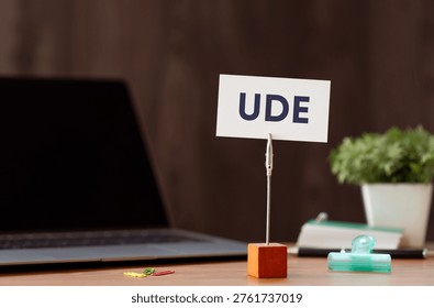 Eye-catching image of UDE text on card. The word stands for Undesirable Effect. Shown with laptop, clips, pen.
