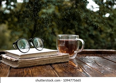 eyeglasses, glass tea Cup and old books on table in garden. Rainy weather day, summer or autumn season. relax time, meditation - Powered by Shutterstock