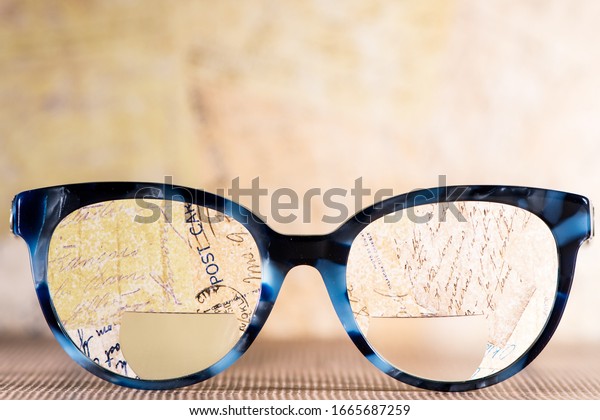 Eyeglasses Glasses with\
Bifocals and Black blue Frame smudged against written letters. \
Blurry Vision\
Concept