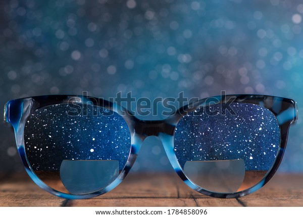 Eyeglasses\
Glasses with Bifocals and Black blue Frame smudged view agaist a\
starry night sky. Blurry Vision\
Concept