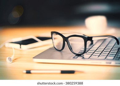 Eyeglasses on laptop keyboard with headphones and diary on wooden table at evening, close up