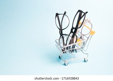 Eyeglasses In A Small Shopping Trolley, Blue Background, Copy Space, Online Buying Glasses And Eyeglass Frames, Online Optics Store