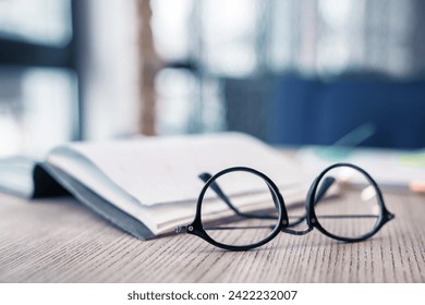 Eyeglasses at the wooden table with notebook on the background. Focus on glasses. Literature, studying, learning process, library concept. Knowledge and wisdom