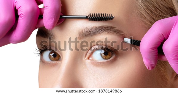 Eyelash artist plucks eyebrows\
with tweezers. Beautiful woman having Permanent Make-up Tattoo on\
her Eyebrows. Professional makeup and cosmetology skin\
care.