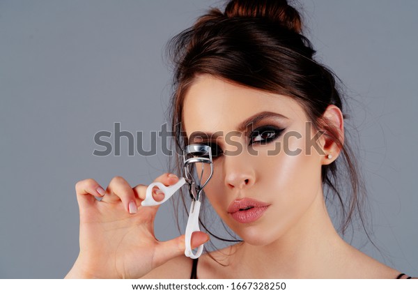 Eyelash curler. Beautiful\
girl using eyelash curler on long eyelashes. Curly eye lashes.\
Portrait of beautiful young woman using beauty tool on curly long\
eyelashes
