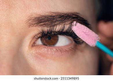 Eyelash Extension. combing the extended eyelashes. A girl with brown eyes does a close-up makeup. Eyelash Care Treatment: eyelash lifting, staining, curling, laminating and extension for lashes.