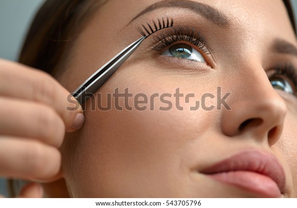 Eyelash Extension. Hand With Tweezers Applying\
Artificial Eyelashes On Beautiful Woman Eyes. Closeup Of Female\
Model Face With Long Fake Eye Lashes. Extremely Long Lashes. High\
Resolution Image