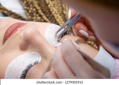 Eyelash Extension Procedure. Woman Eye with Long false Eyelashes. Close up macro shot of tweezers in hands of beautican