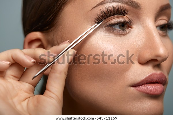 Eyelashes. Beautiful Woman Applying False\
Eyelashes With Tweezers. Closeup Of Young Female Model Face With\
Professional Facial Makeup, Smooth Skin And Long Black Thick Eye\
Lashes. High\
Resolution