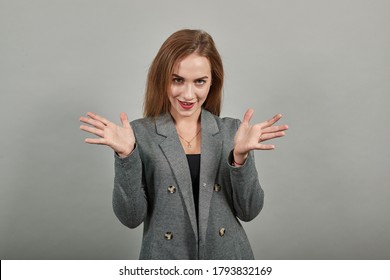 Eyes Open Wide, Surprised Look, Delightfully Plants Hands, Showing Palms Spreading Fingers, Emotional, Shocked With News. Arms For Hug, So Happy To See You. Young Attractive Woman, Dressed Gray Jacket