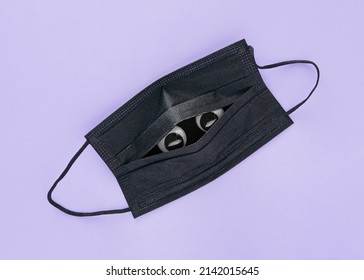 Eyes Peek From The Anti-covid Mask On Isolated Purple Background. Minimal Abstract Post-pandemic Dystopian Concept. The Idea Of Stress Disorder, Fear, Mental Health, Anxiety Or Brain Fog. Flat Lay.