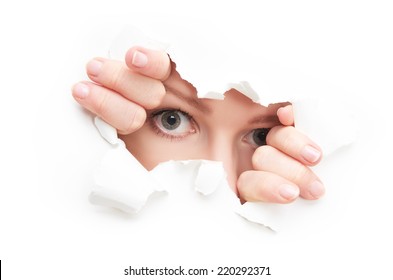 eyes of a young curious woman peeking through a  hole torn in white paper poster