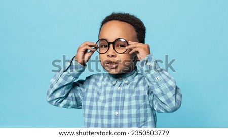 Eyesight. Portrait of little black boy wearing eyeglasses looking at camera, standing on blue studio background. Kids eyes health and sight correction concept