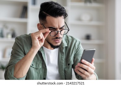 Eyesight Problems Concept. Young Arab Man In Eyeglasses Looking At Smartphone Screen And Frowning, Millennial Guy Trying To Read Message, Suffering From Astigmatism And Bad Vision, Closeup Shot - Shutterstock ID 2143217521