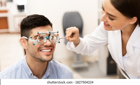 Eyesight Test, Medical Examination Concept. Portrait of smiling specialist female optometrist checking the eye vision of male client with trial frame. Woman examining man with diagnostic tool - Powered by Shutterstock