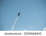 An F-16 fighter jet performing a vertical climb with smoke trails in a clear blue sky.The aircraft is silhouetted against a vibrant blue sky whirling while vertical climbing