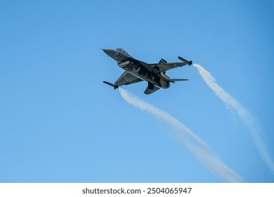 F-16 High-Speed Pass. A Solo Turk F-16 fighter jet in mid-air, performing a high-speed pass with smoke trails trailing behind it. The jet is angled upwards, creating a sense of dynamism and speed - Powered by Shutterstock