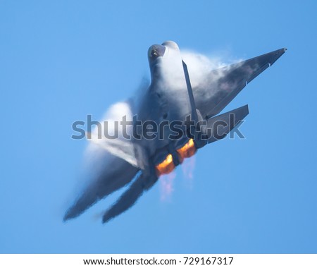 F-22 Raptor in a high-G maneuver, with afterburners on, and condensation clouds and streaks around the plane.