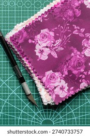 Fabric patchwork quilting patterned quilting squares on a green cutting mat with a craft knife background backdrop.