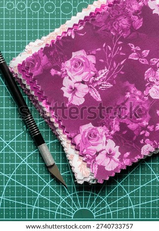Fabric patchwork quilting patterned quilting squares on a green cutting mat with a craft knife background backdrop.