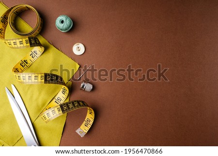 Fabric and sewing tools for needlework on a brown background, flat flat, top view, copy space. Creating fashion clothing concept. Horizontal background for advertising or packaging.