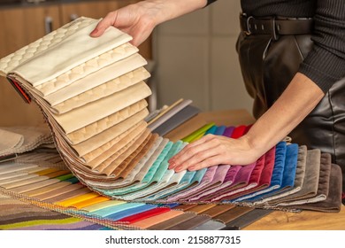 Fabric Swatches In Different Colors Are Stacked For Selection. A Woman Chooses Upholstery Colors For Furniture And Interiors. Touches The Texture Of The Fabric, Hands On The Material Close-up.