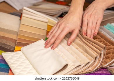 Fabric Swatches In Different Colors Are Stacked For Selection. A Woman Chooses Upholstery Colors For Furniture And Interiors. Touches The Texture Of The Fabric, Hands On The Material Close-up.