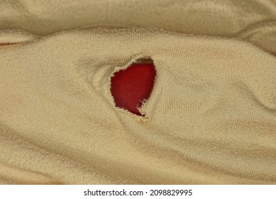 fabric texture from a piece of brown crumpled clothing with a red torn hole