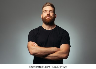 Fabulous at any age. Portrait of charismatic muscular 30-year-old man standing over dark gray background. Perfect haircut. Rocker, biker, hipster style. Hands crossed. Copy-space. Studio shot