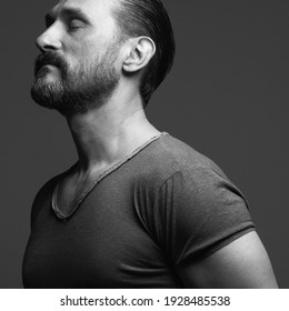 Fabulous At Any Age. Profile Portrait Of Charismatic Muscular 45-year-old Man Standing Over Dark Gray Background. Hair Brushed Back. Rocker, Biker Style. Close Up. Black And White Studio Shot